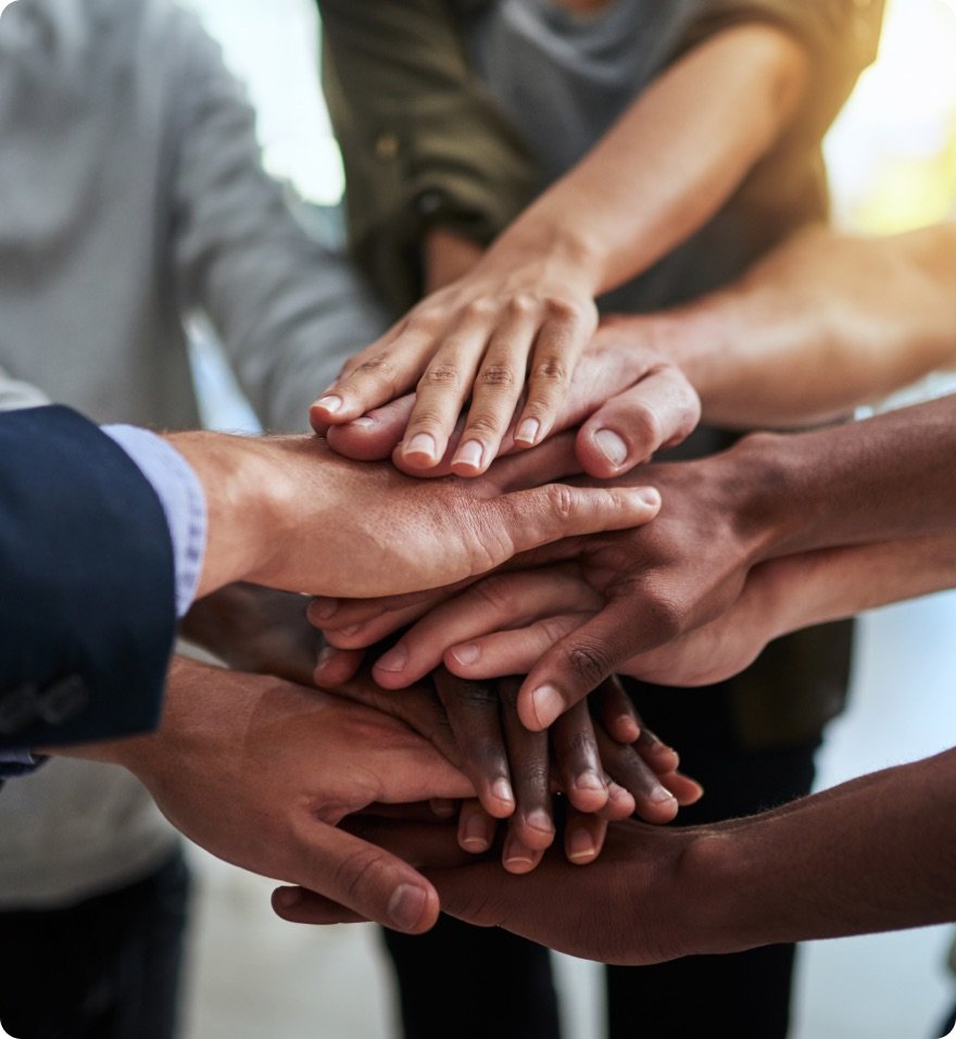 Profissionais unindo as mãos sobre uma mesa de reunião, representando trabalho em equipe e colaboração.